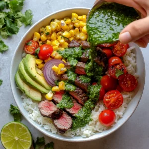 Steak Avocado and Roasted Corn Bowl with Cilantro Cream Sauce:Bowl filled with sliced steak, avocado, cherry tomatoes, roasted corn, red onion, and white rice, topped with a drizzle of green cilantro cream sauce.